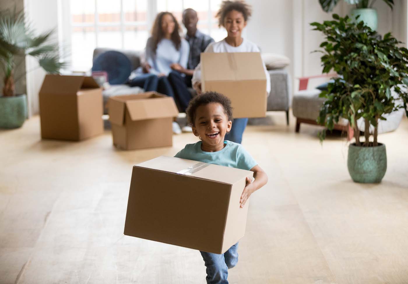 Family of four smiling, carrying moving boxes into their new house after home inspection services were scheduled 